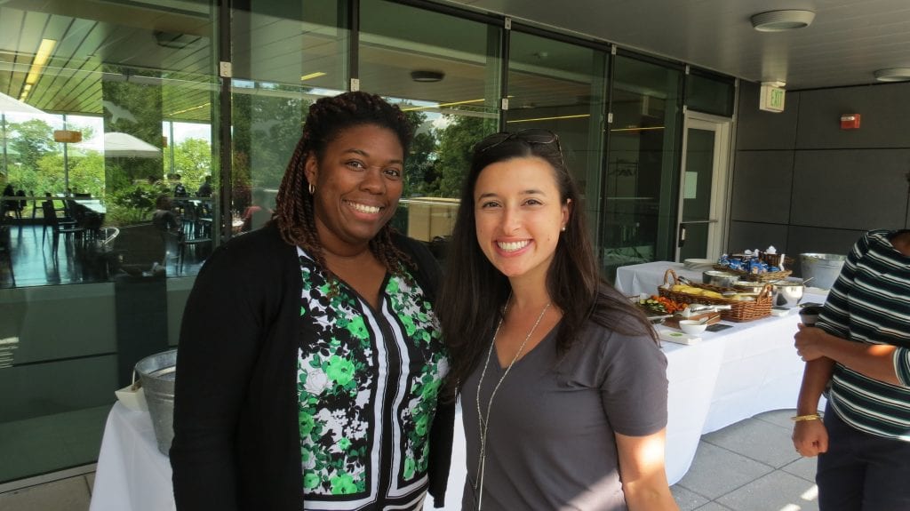 Photo of CIE scholar Jinelle Wint and CIE administrator Julianna Prior at the 2017 CIE welcome barbecue. Jinelle and Julianna are smiling and standing in front of an event table at the Simons Center Safe containing food and beverages. It is a sunny dat